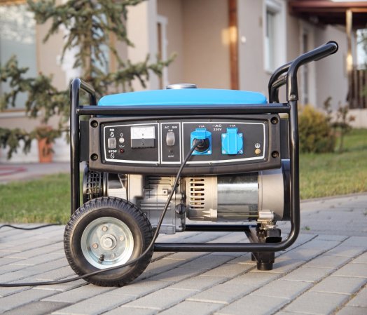 A blue portable generator is in front of a house.