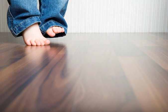A child's bare feet are lightly touching the wooden floor.