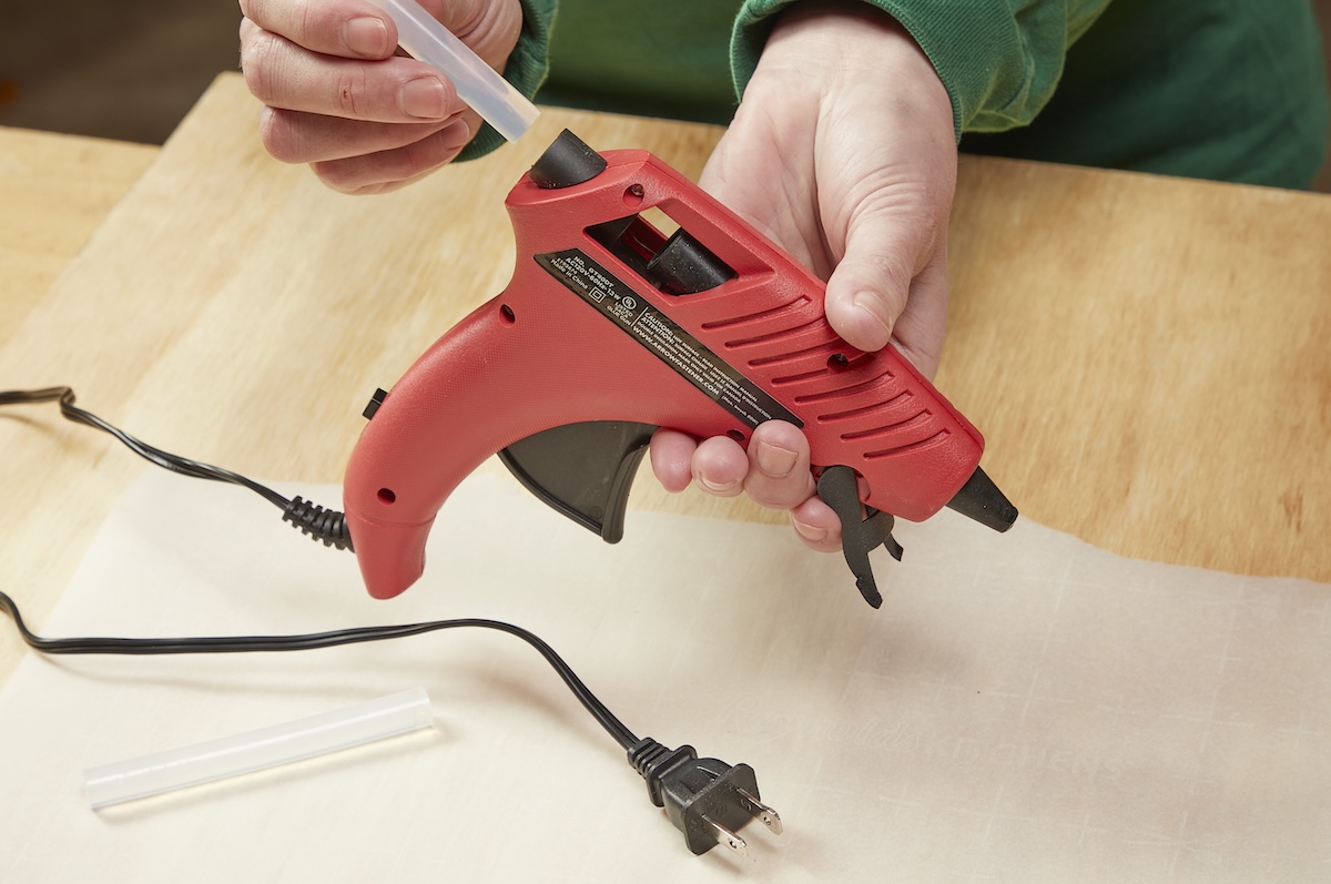 A DIYer loading a glue stick into a glue gun for home improvement projects and repairs.