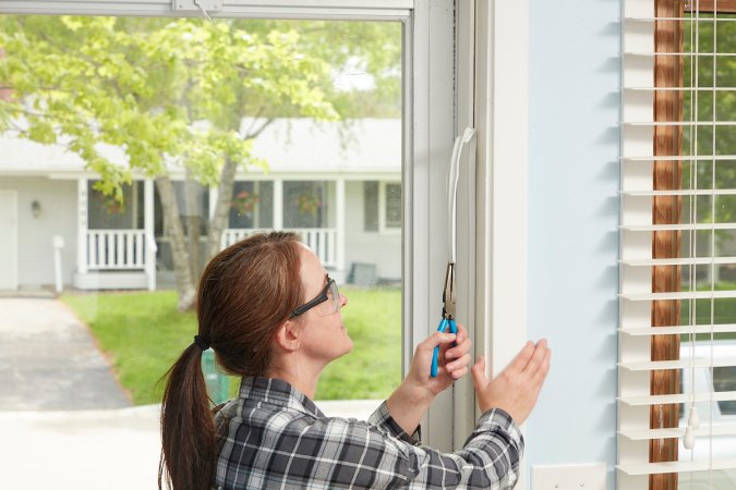 Woman uses needle-nose pliers to pull weather stripping off from around a door.
