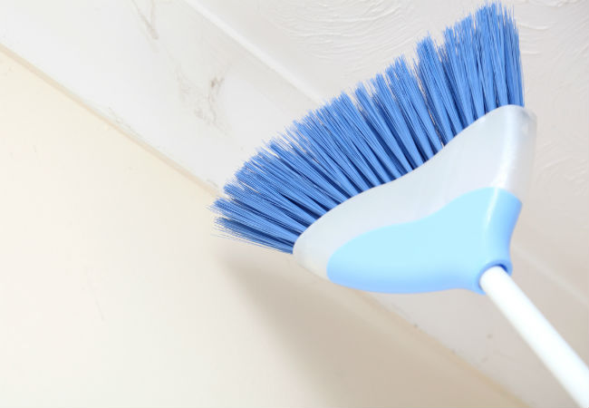 Using a broom to dust a popcorn ceiling.