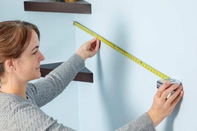 Woman extends a tape measure from the corner of the room to measure the wall.