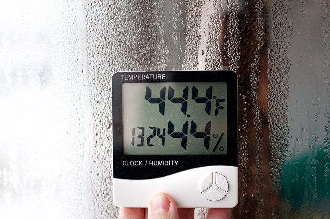 Electric humidity meter held up near window with condensation measures moisture in air.