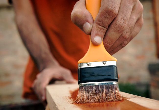 Man holding brush, spreading shellac on a wood workpiece.