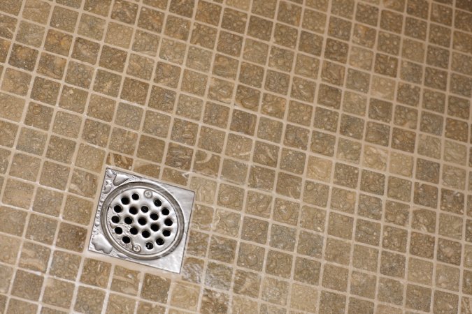A drain at the bottom of a shower with beige tiles.