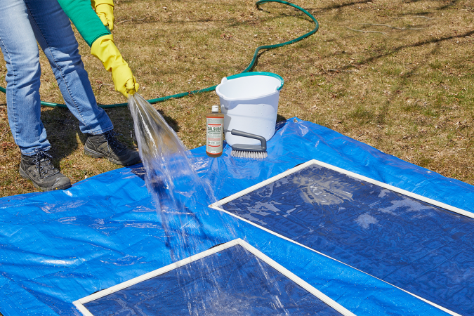 A homeowner using a hose to rinse window screens.